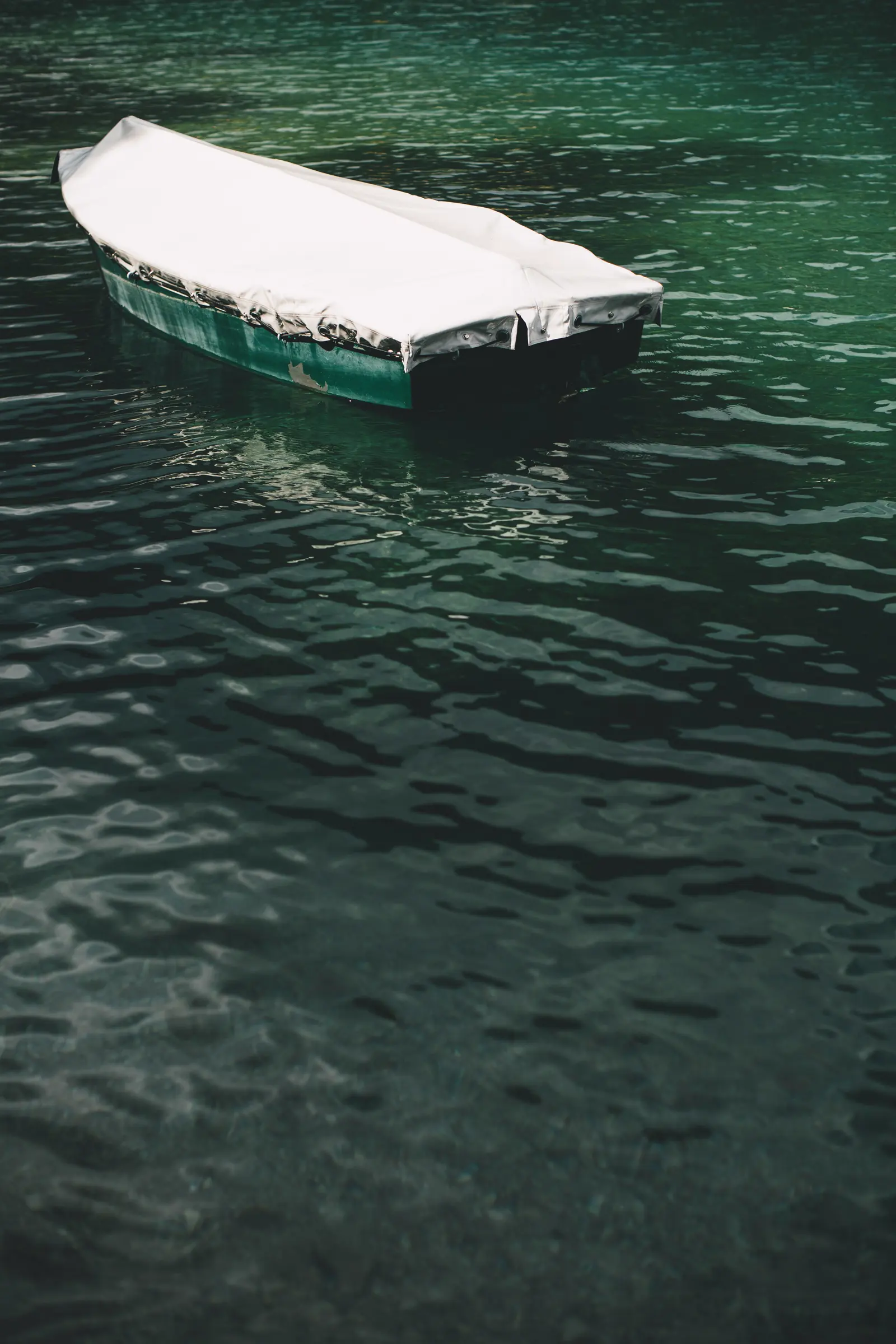 Abgedecktes grünes Ruderboot auf dem grünen Wasser des Plansees, von oben fotografiert