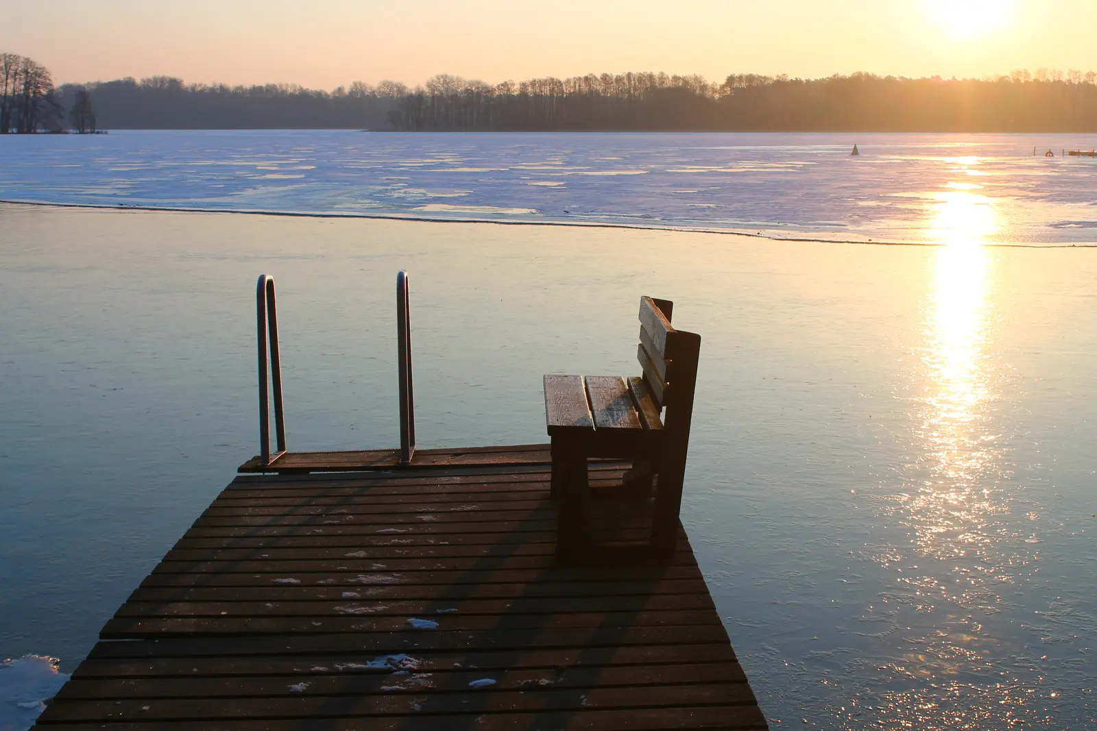 Hölzerner Badesteg mit Leiter und Bank im Gegenlicht an einem See in Mecklenburg